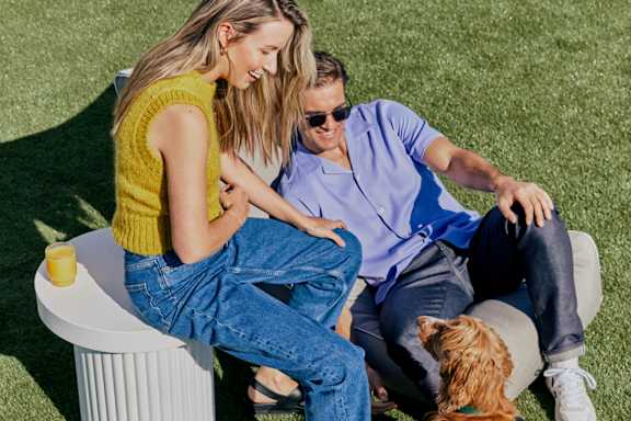A man and woman sitting on a white bench with a dog.