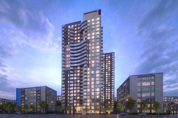 A modern high-rise building stands tall among other buildings in a cityscape at dusk.