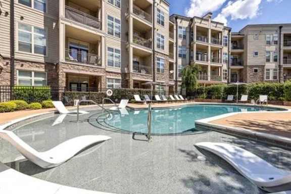 A swimming pool surrounded by white lounge chairs in front of apartment buildings.