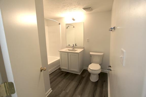 A white toilet sits in a small bathroom with a white cabinet and a mirror.