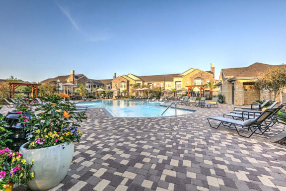 a swimming pool with lounge chairs and flowers in front of a house at Waterstone at Cinco Ranch, Katy, TX, 77450