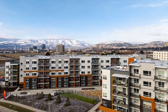 Apartment buildings with orange and grey accents are in the foreground with snow covered mountains in the background.