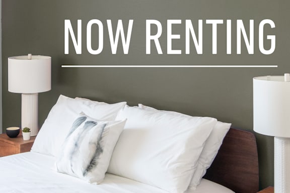 A bedroom with a bed, nightstand, and lamp advertising The Oaks Apartments.