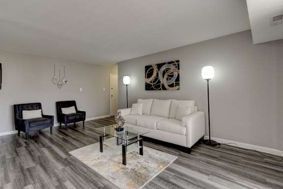 A living room with a white couch, a black chair, and a glass coffee table.
