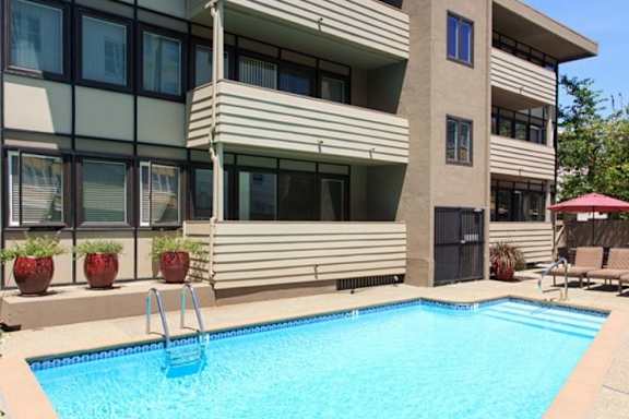 A swimming pool in front of a building with a red umbrella.