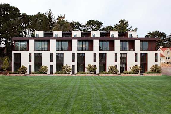 A large white building with black trim and windows sits on a lush green lawn.