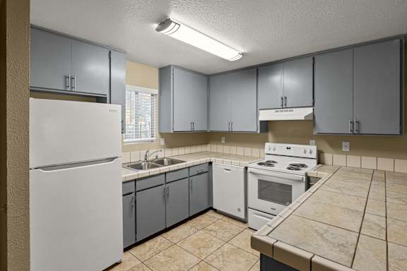 A kitchen with a white refrigerator, white oven, and grey cabinets. at Cedar Park Apartments, Chico
