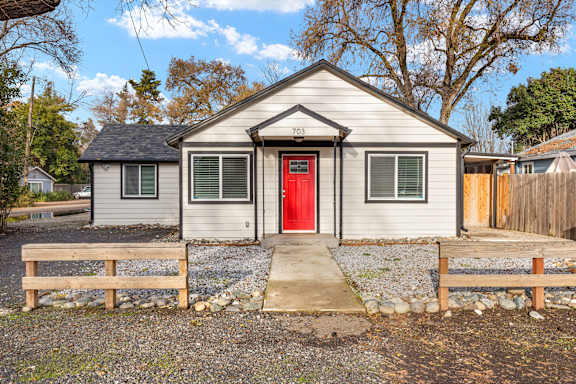 A small house with a red door is surrounded by a gravel area and wooden fences.at OSM Properties Homes & Apartments, Chico, 95926