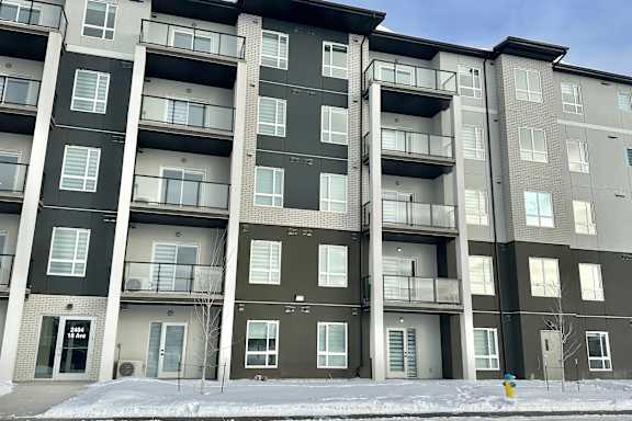 Apartment building with grey and white exterior and snow on the ground.