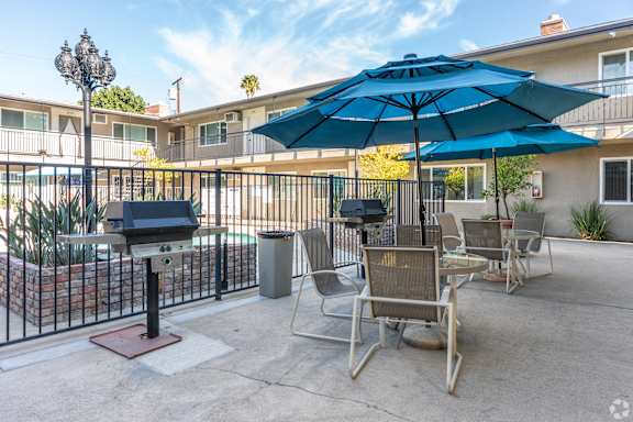 A patio with chairs, an umbrella, and a grill.