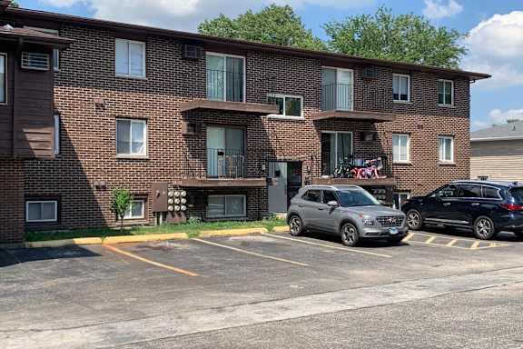 A parking lot in front of a brown brick apartment building with two cars parked.