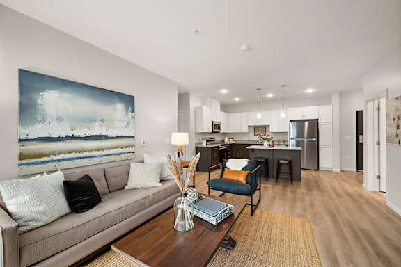 A modern living room with a large painting on the wall and a beige sofa at The Landing at Amber Fields Apartments, Minnesota
