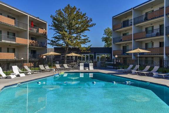A swimming pool in front of apartment buildings with sun loungers and umbrellas.