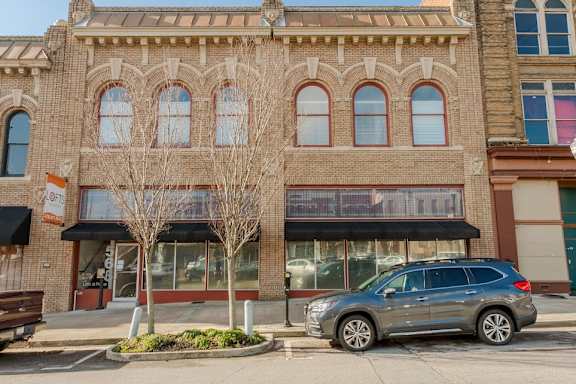 A tree in front of a building with a car parked in front of it.