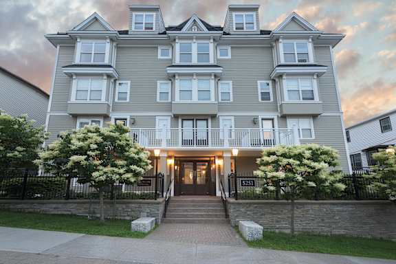 A large, grey apartment building with a black fence and a stone wall in front.