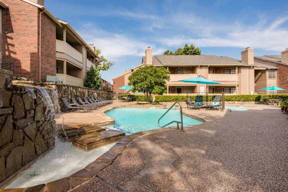 Swimming pool with stone waterfall and lounge seating at Ashwood Park Apartments, Texas