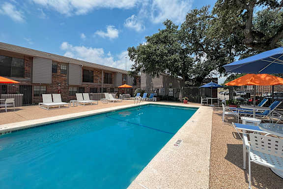 Outdoor pool with umbrellas and lounge seating at Autumn Chase Apartments, San Marcos