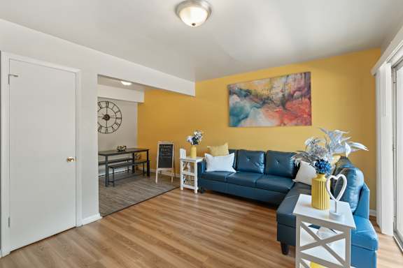 A living room with a blue couch and a painting on the wall.
