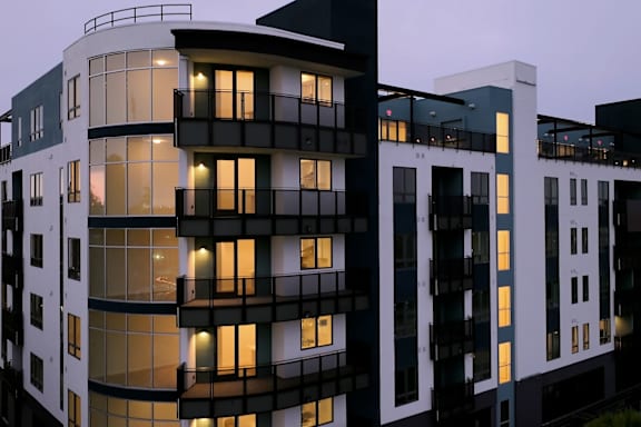 A modern building with balconies and large windows is illuminated from within.