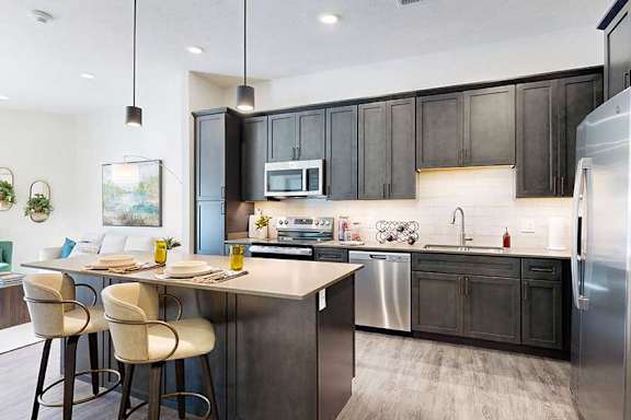 a modern kitchen with a stainless steel appliances, quartz countertops, a light tile backsplash, dark wooden cabinets, and a large central island