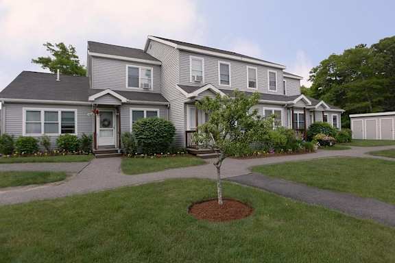 A grey house with a tree in front of it.