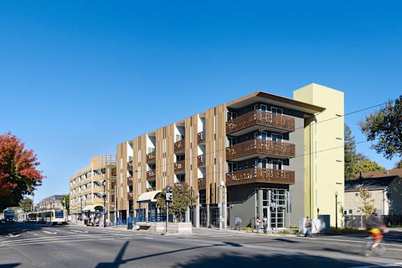 A modern building with balconies is situated on a street corner.