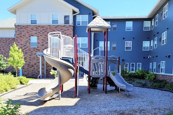 A playground with a slide and a swing set in front of a building.