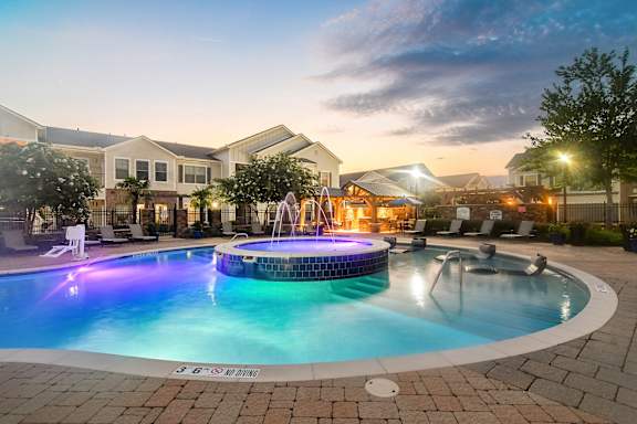 a swimming pool at night with houses in the background