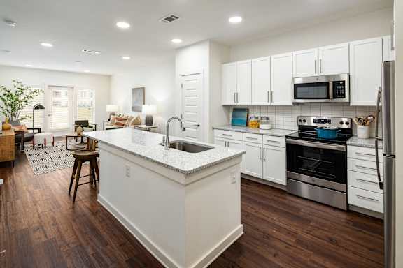 an open kitchen and living room with white cabinets and a counter top