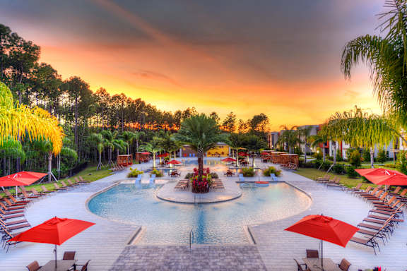A beautiful outdoor swimming pool area with red umbrellas and loungers.