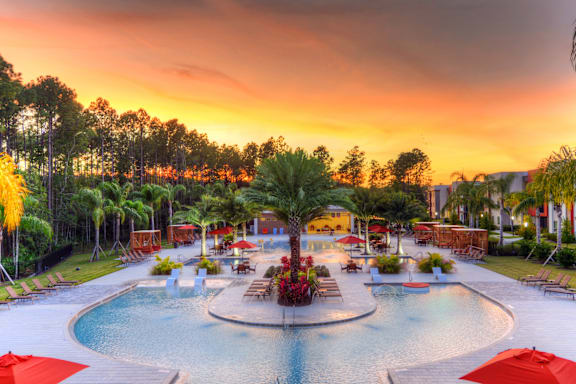 A beautiful outdoor swimming pool area with red umbrellas and lounge chairs.