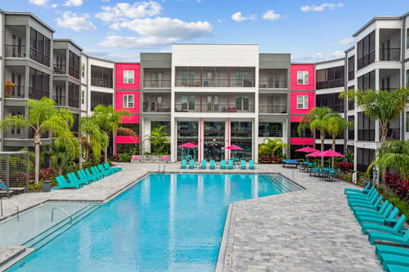 A large swimming pool surrounded by lounge chairs and umbrellas in front of a modern building.
