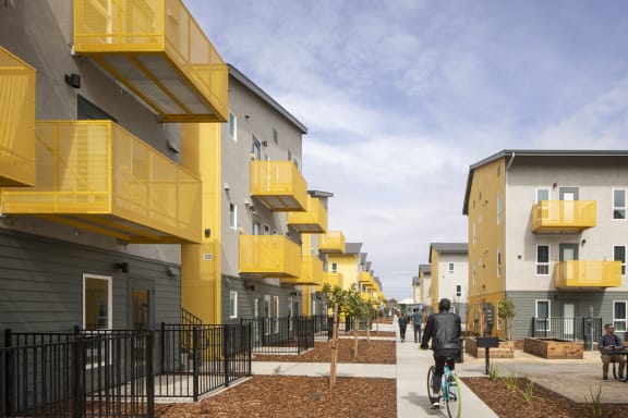 a row of multifamily buildings with yellow balconies and people walking and biking