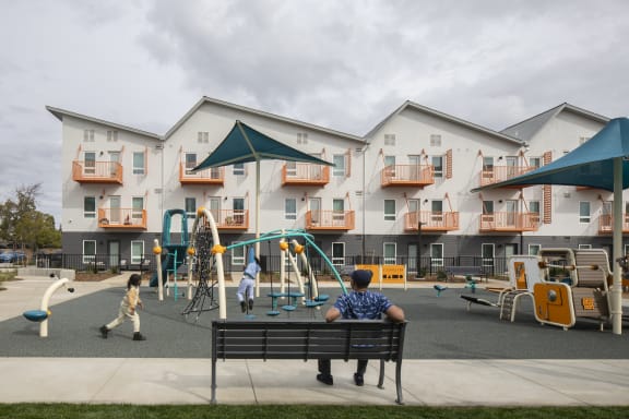a man sitting on a bench in front of Mutual Housing on the Boulevard playground