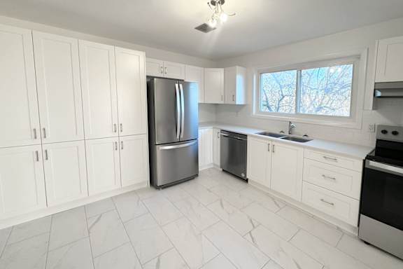 A kitchen with white cabinets and marble flooring.
