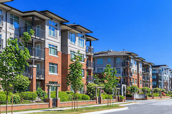 A row of modern apartment buildings with balconies and trees in front.