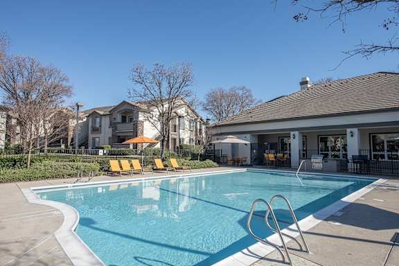 A swimming pool in front of a house with a patio and sun loungers.