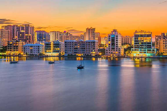 A city skyline at dusk with buildings reflecting on the water.