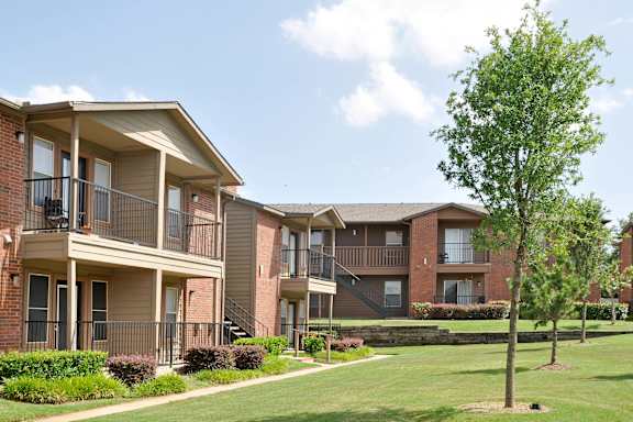 A tree stands in a grassy area in front of apartment buildings.
