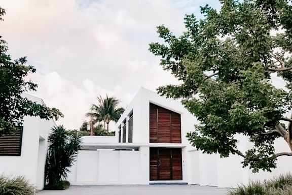 A white house with a red door and a tree in front.