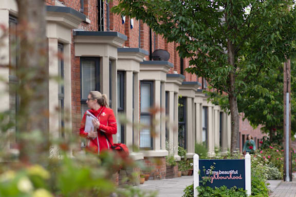 A woman in a red coat is walking down a sidewalk past a sign that says "my beautiful garden".