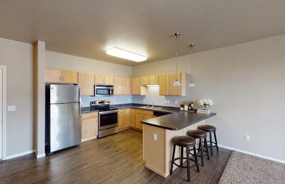A kitchen with a refrigerator, microwave, oven, and bar stools.