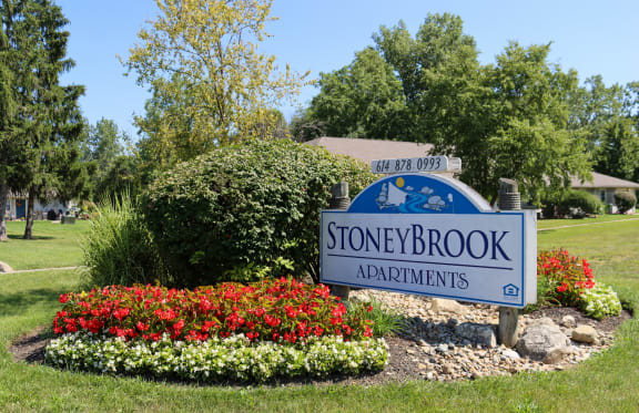 the sign for stone brook apartments in front of a flower garden