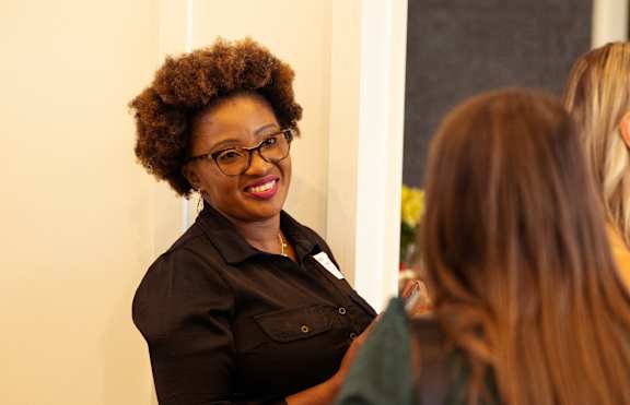 A woman with glasses and a black shirt is smiling at someone.