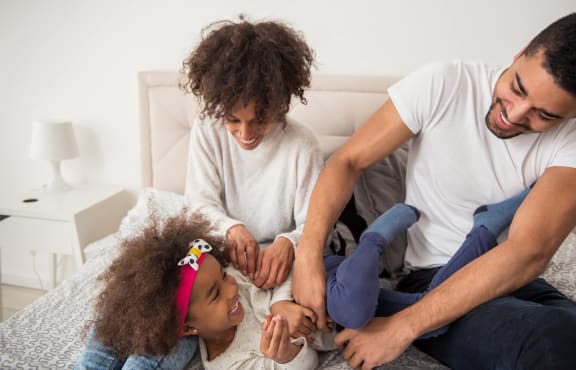 a young family sitting on the bed playing with their daughter