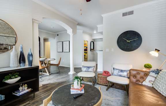 A living room with a brown leather couch, a round table, and a large clock on the wall.