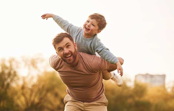 A man is carrying a child on his back in a park.