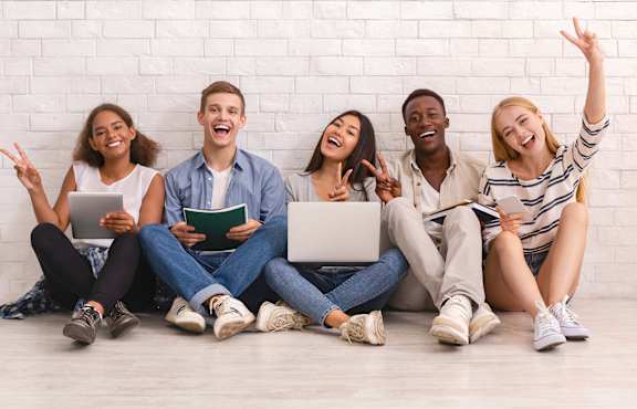 A group of five people are sitting on the floor in front of a white brick wall.