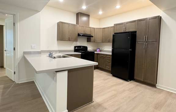 A kitchen with a black refrigerator and brown cabinets.
