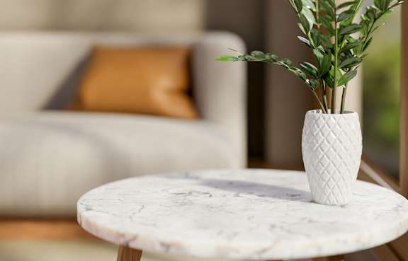 A white vase with a plant in it sits on a marble table.